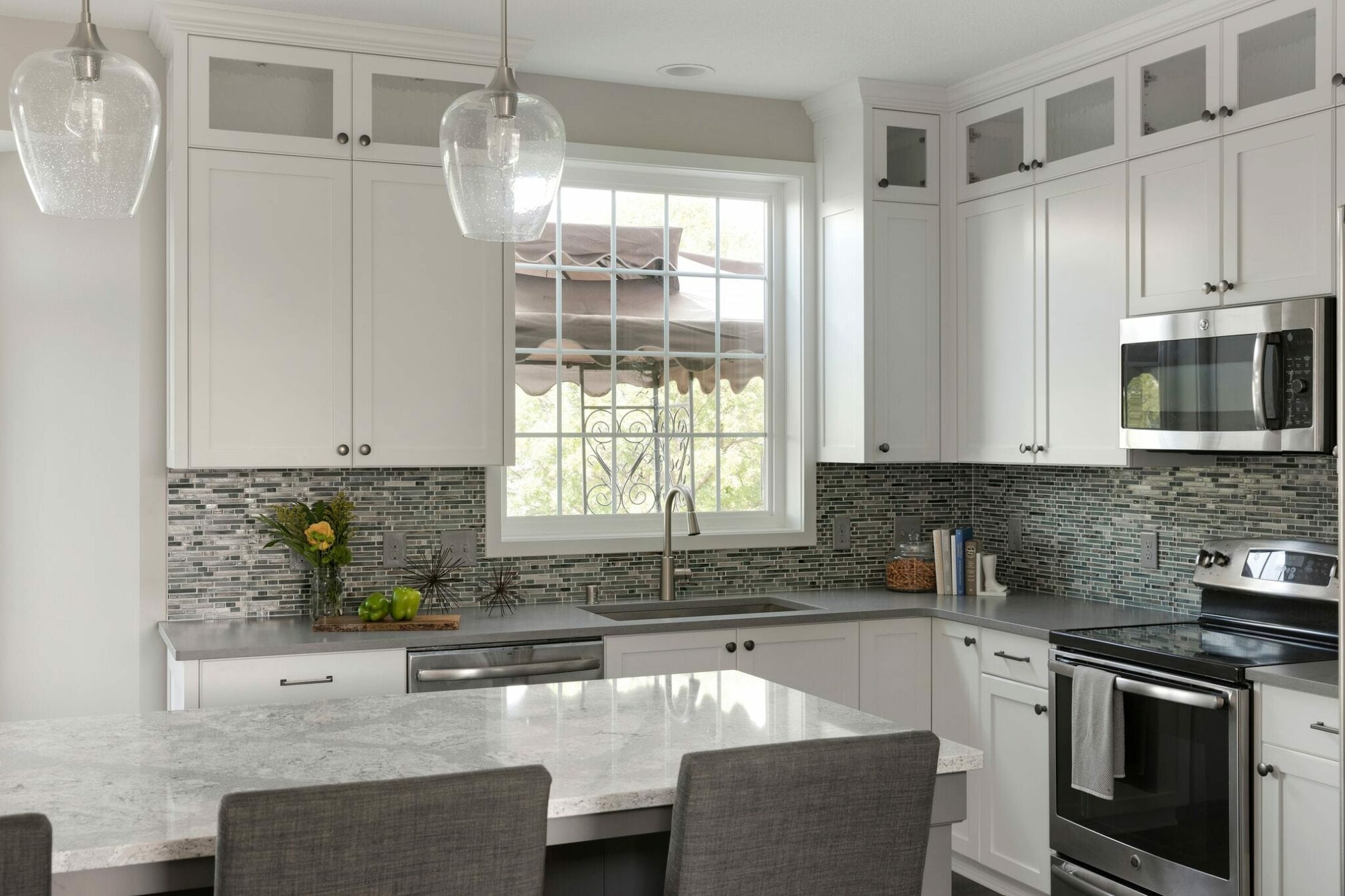 White kitchen remodel with gray backsplash and gold and glass light fixtures. 