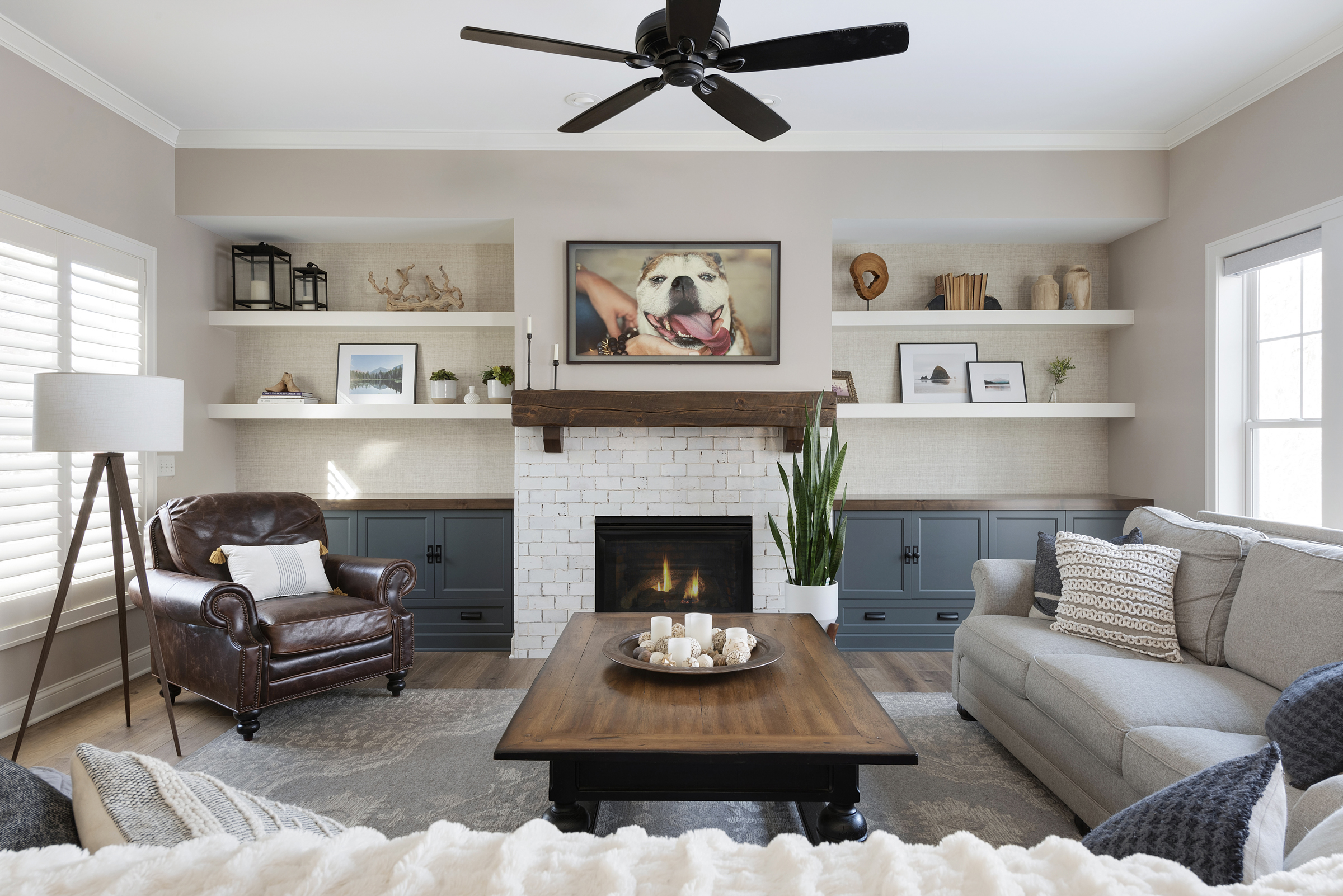 Living room with multiple open shelves, fireplace, ceiling fan, and picture of a dog.