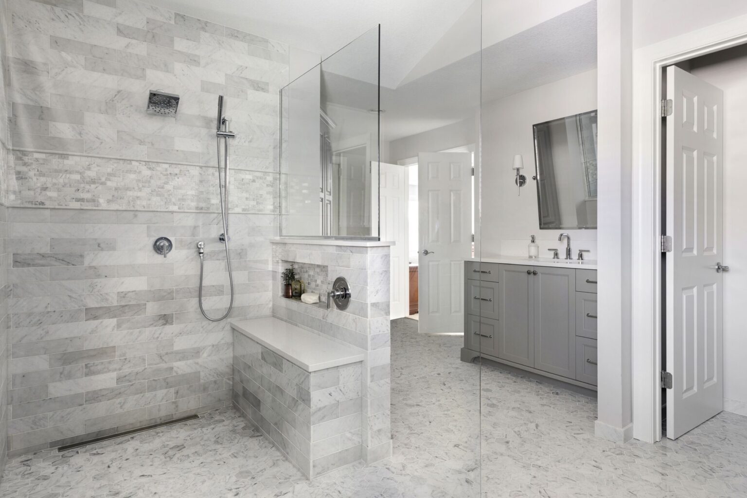 Walk-in shower with gray tile, bench, and built-in shelf.