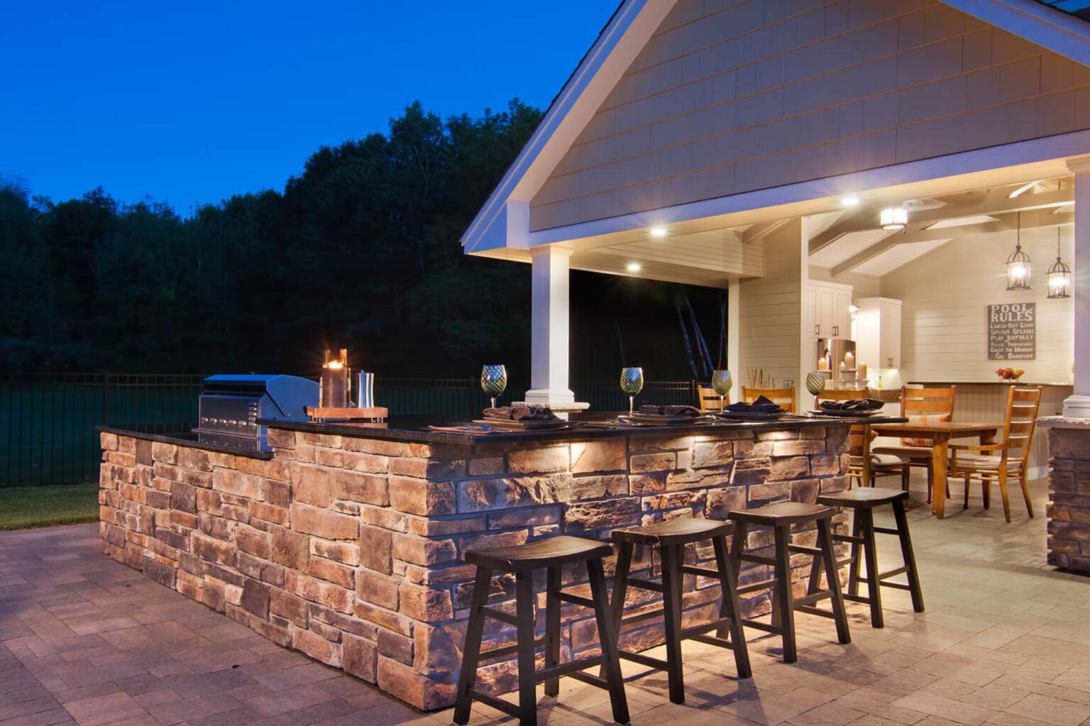 Blended indoor and outdoor living space with a grill and bar seating against a night sky. 