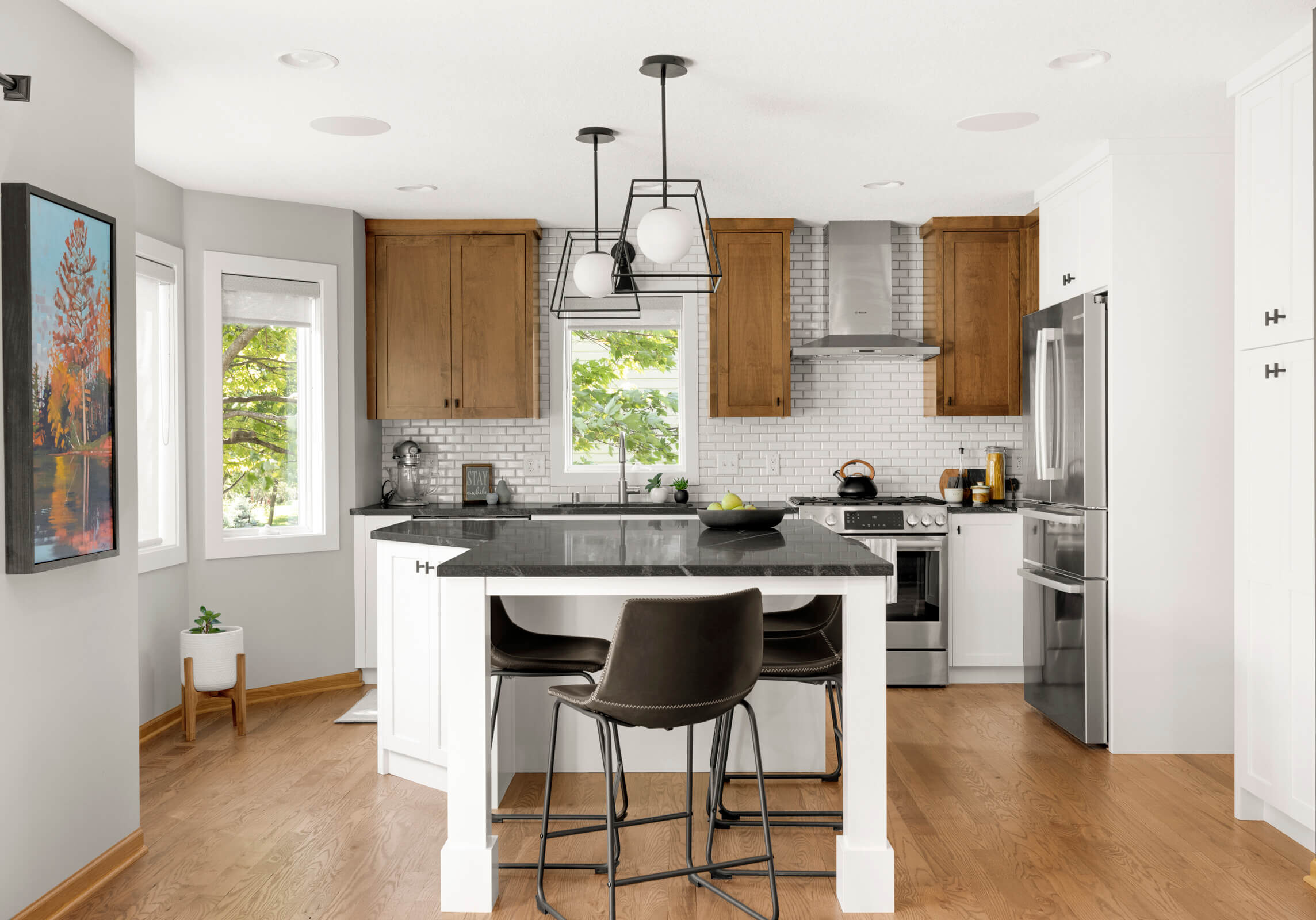 Remodeled kitchen with hardwood flooring and cabinety and black pendant lights.